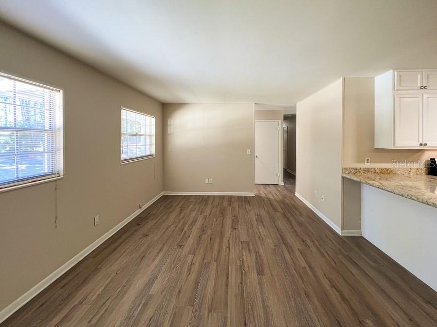 An empty room with wood-look flooring, beige walls, two windows, and a kitchen counter — 2110 NW 54TH TERRACE, GAINESVILLE, FL