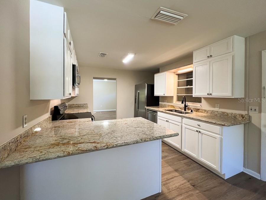 A kitchen with white cabinets, granite countertops, stainless steel appliances, and wood-look flooring — 2110 NW 54TH TERRACE, GAINESVILLE, FL