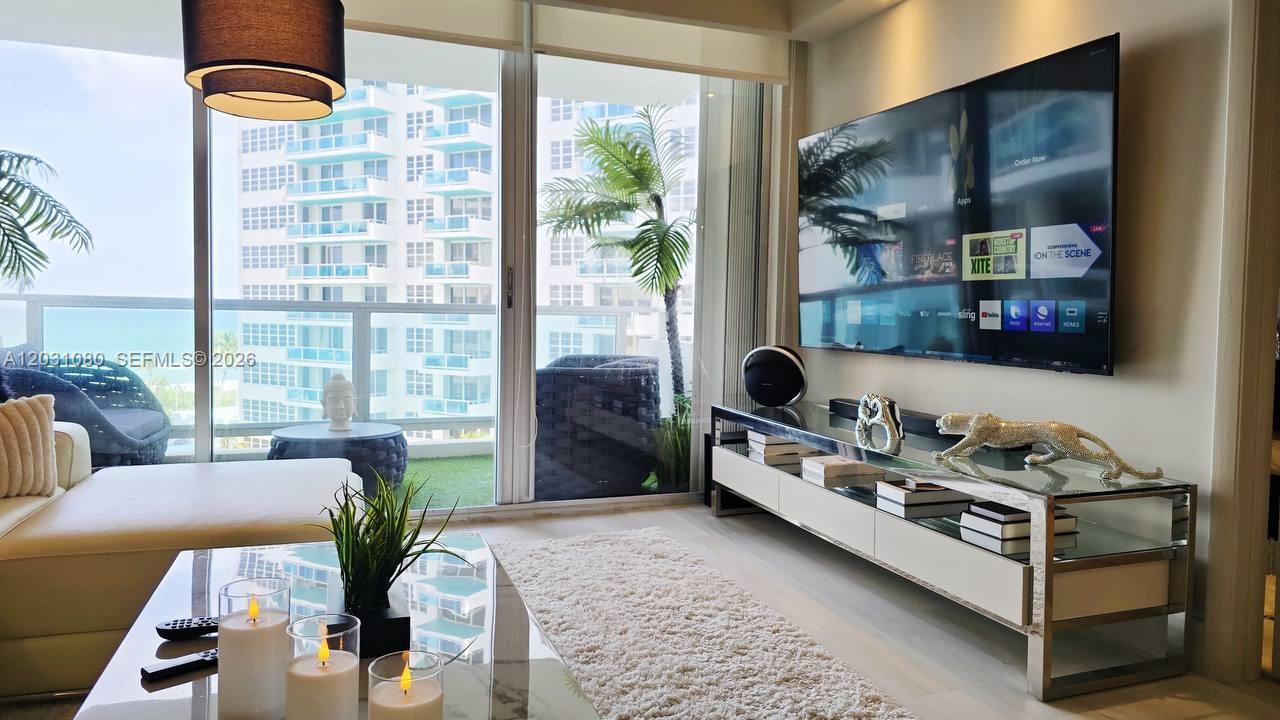 A modern living room features a large television, glass media console, and balcony with ocean views — 5151 Collins Ave # 726, Miami Beach FL 33140, MIAMI BEACH, FL