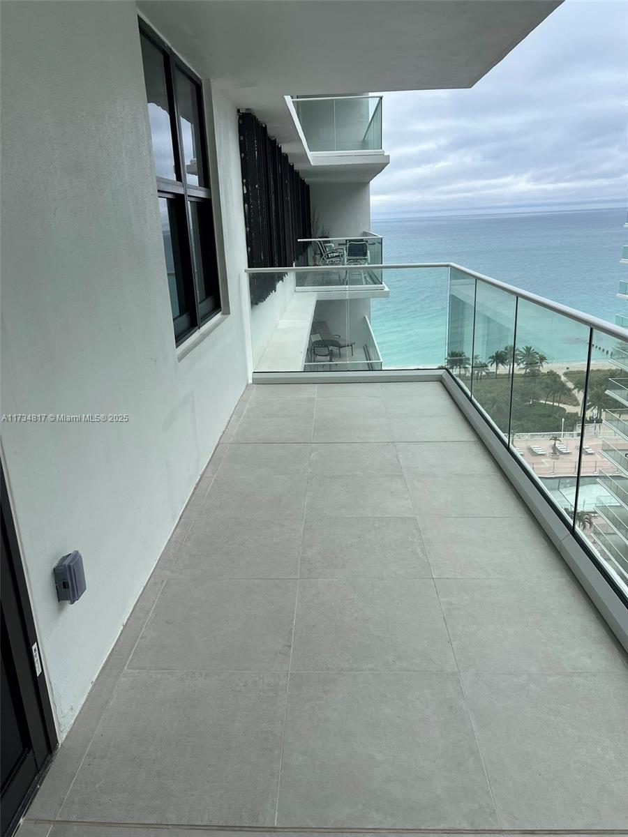 A balcony with large gray floor tiles and a glass railing overlooks the ocean — 9801 Collins Ave # 17J, Bal Harbour FL 33154, BAL HARBOUR, FL
