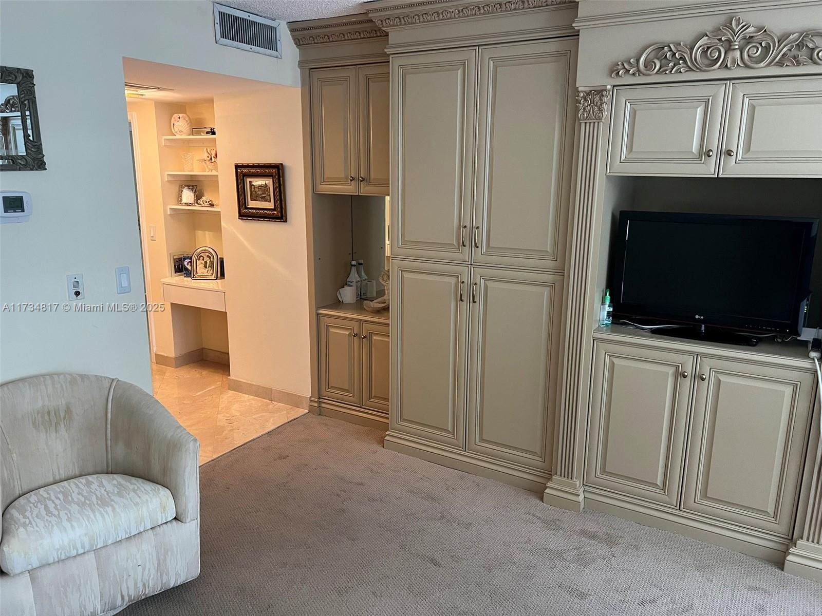 A living room features beige built-in cabinetry, a television, and a carpeted floor — 9801 Collins Ave # 17J, Bal Harbour FL 33154, BAL HARBOUR, FL