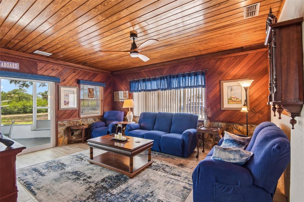 A living room features wood-paneled walls and ceiling, blue furniture, and a stone base — 8212 HAYWARD LANE, PORT RICHEY, FL