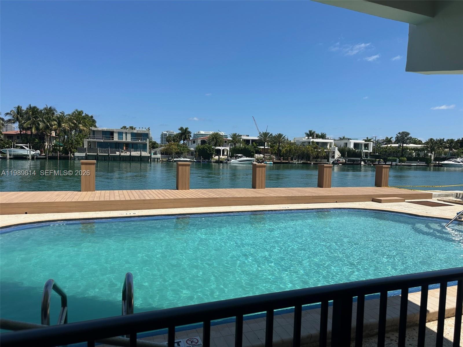 A swimming pool sits in front of a wooden dock overlooking a canal with houses — 9341 E Bay Harbor Dr # 6C, Bay Harbor Islands FL 33154, BAY HARBOR ISLANDS, FL