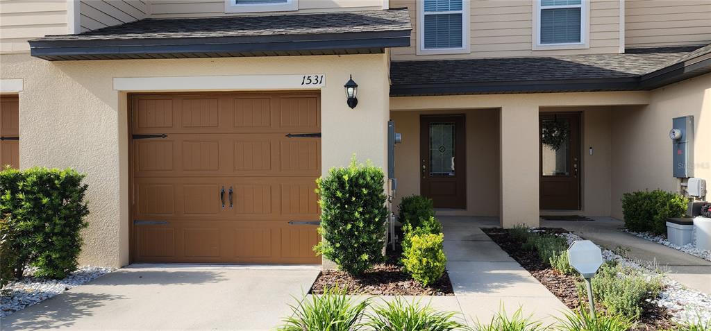 A tan townhouse exterior features a brown garage door, a front entrance, and landscaping — 1531 WYNFORD CIRCLE, TAVARES, FL