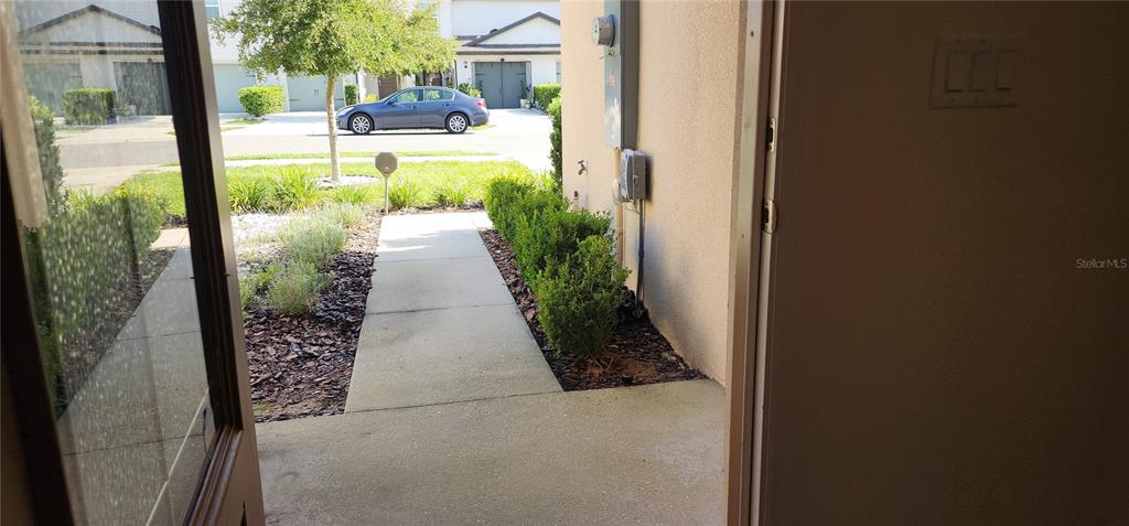 A view from an open doorway looking out onto a concrete walkway and landscaped yard — 1531 WYNFORD CIRCLE, TAVARES, FL
