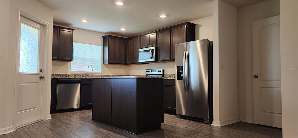 A kitchen features dark wood cabinets, granite countertops, stainless steel appliances, and a central island — 1531 WYNFORD CIRCLE, TAVARES, FL