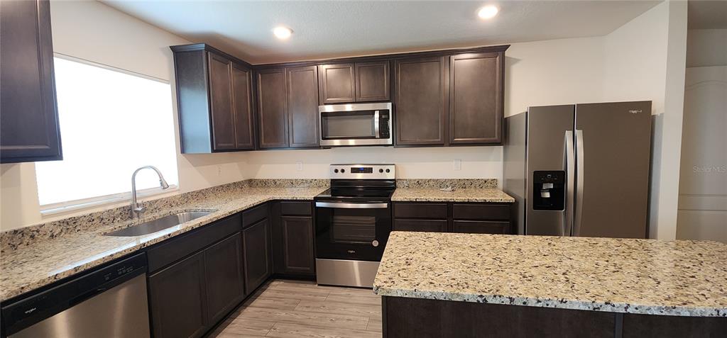 A kitchen features dark wood cabinets, granite countertops, stainless steel appliances, and wood-look flooring — 1531 WYNFORD CIRCLE, TAVARES, FL