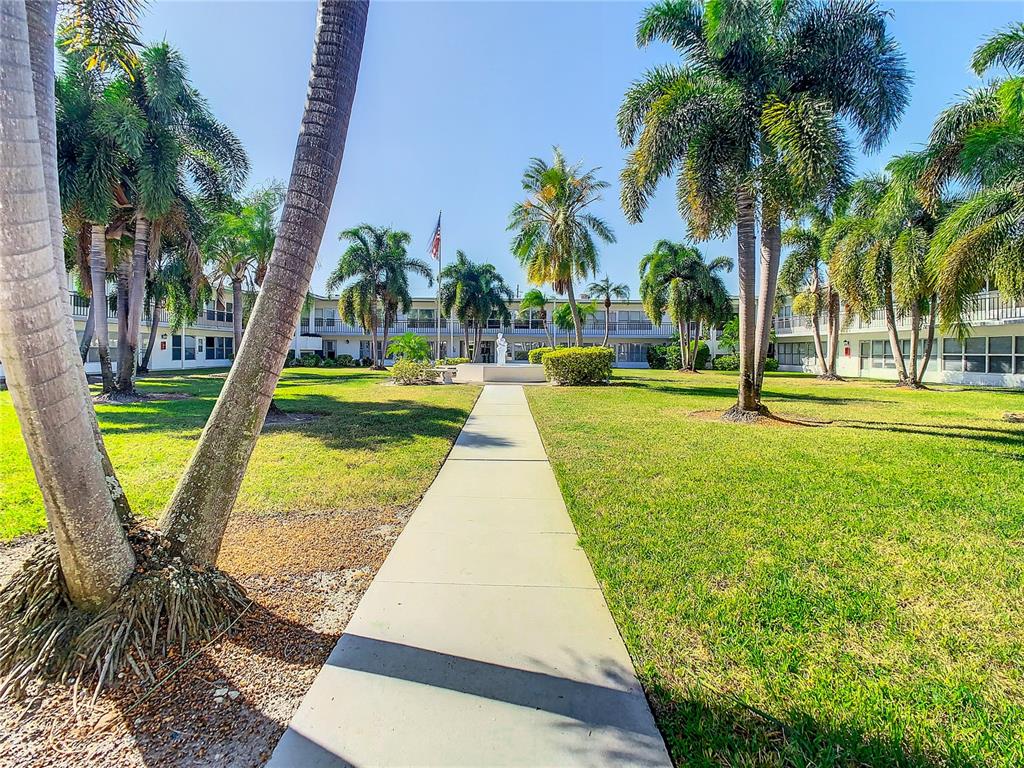 A concrete walkway leads through a grassy courtyard toward a two-story building with palm trees — 3100 HARTFORD STREET N UNIT 227, ST PETERSBURG, FL