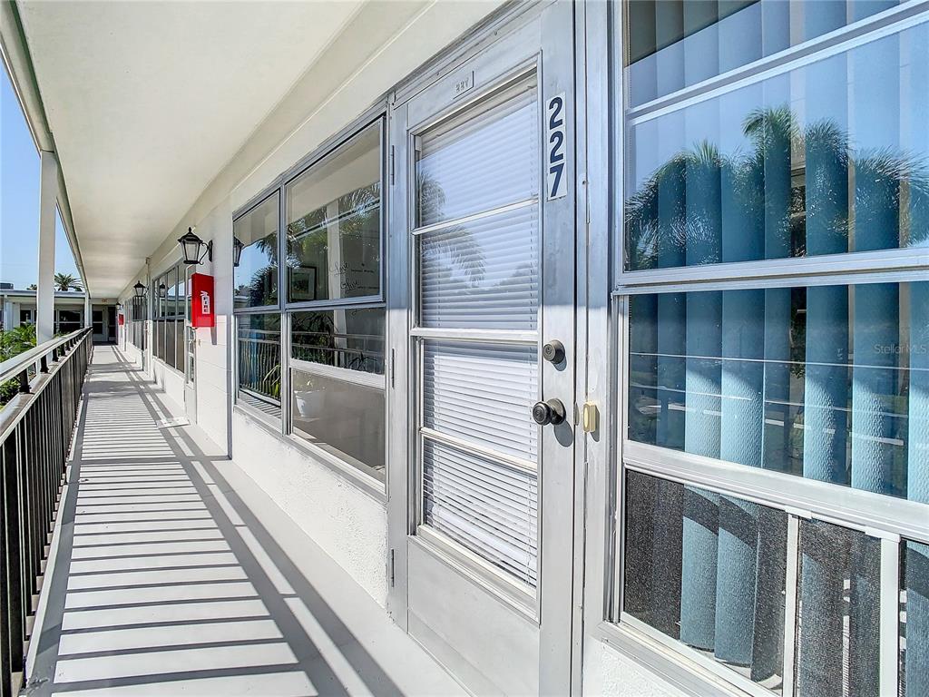 An exterior walkway features a row of apartment doors with glass panels and metal railings — 3100 HARTFORD STREET N UNIT 227, ST PETERSBURG, FL