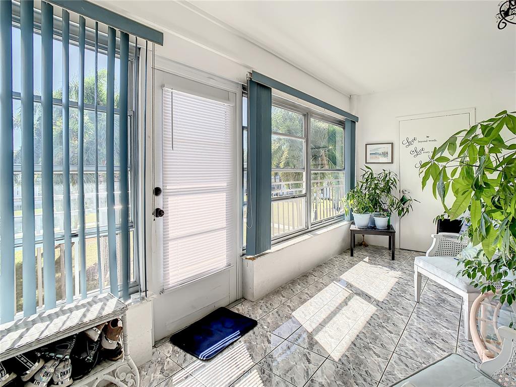 A sunroom features tile flooring, large windows with vertical blinds, and a glass-paneled exterior door — 3100 HARTFORD STREET N UNIT 227, ST PETERSBURG, FL