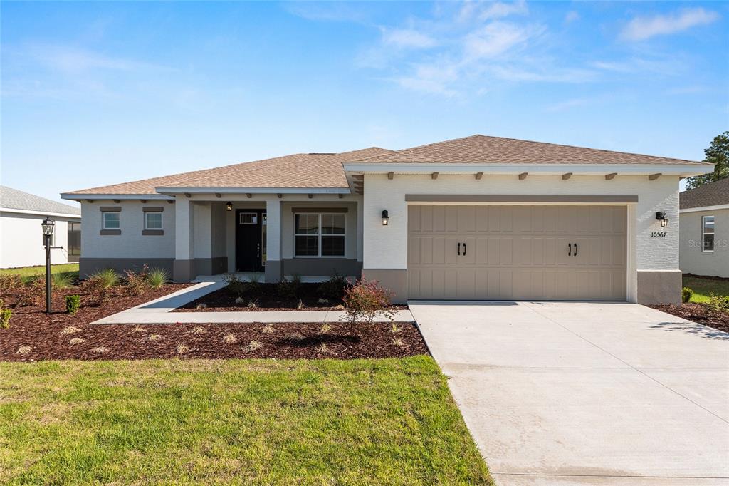 A single-story house features a tan garage, white stucco walls, and a brown shingled roof — 10567 SW 101ST LANE ROAD, OCALA, FL