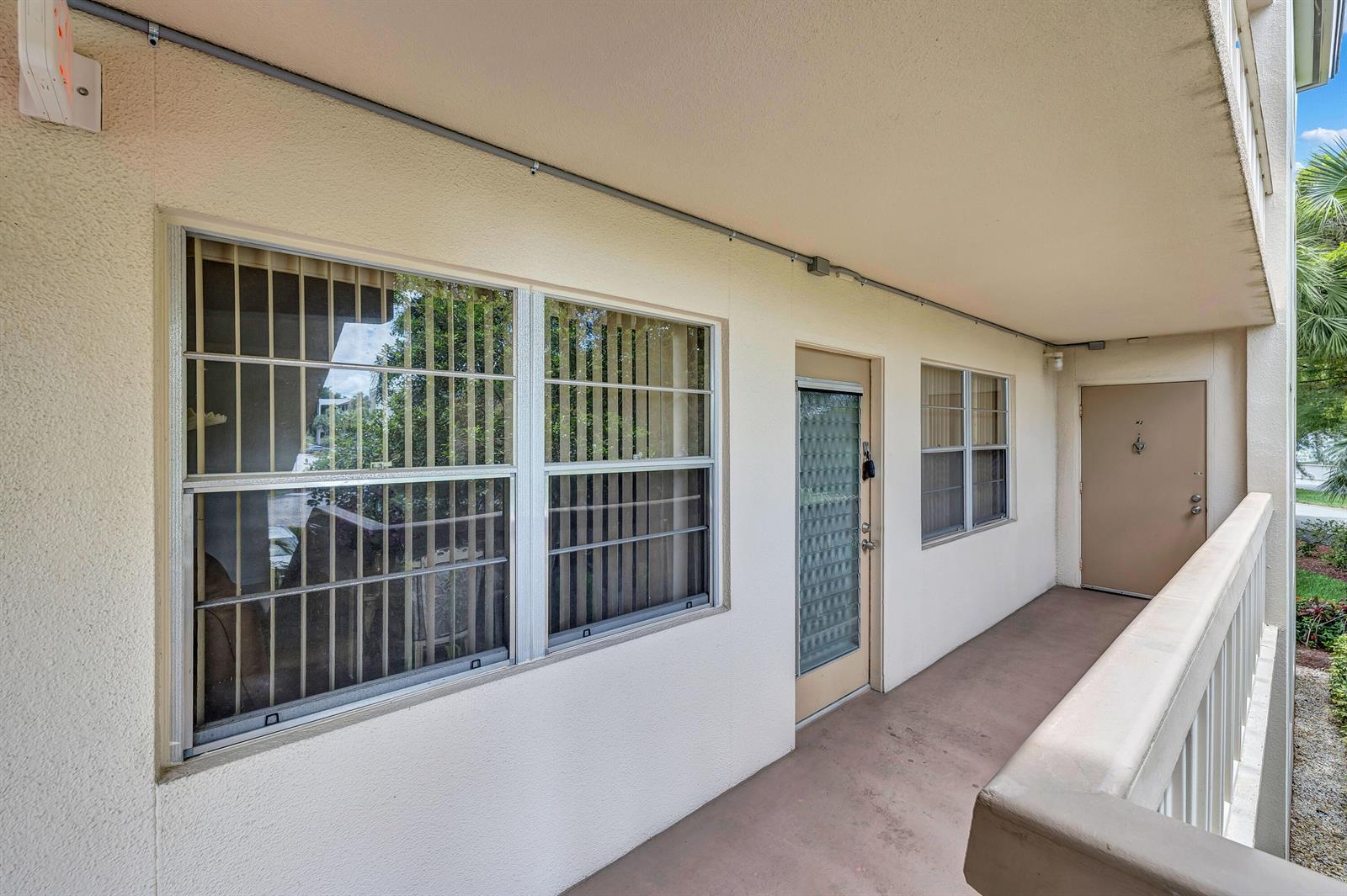An exterior view of a building walkway featuring windows, a glass door, and a solid door — 1902 Bermuda Circle # L2, Coconut Creek FL 33066, COCONUT CREEK, FL