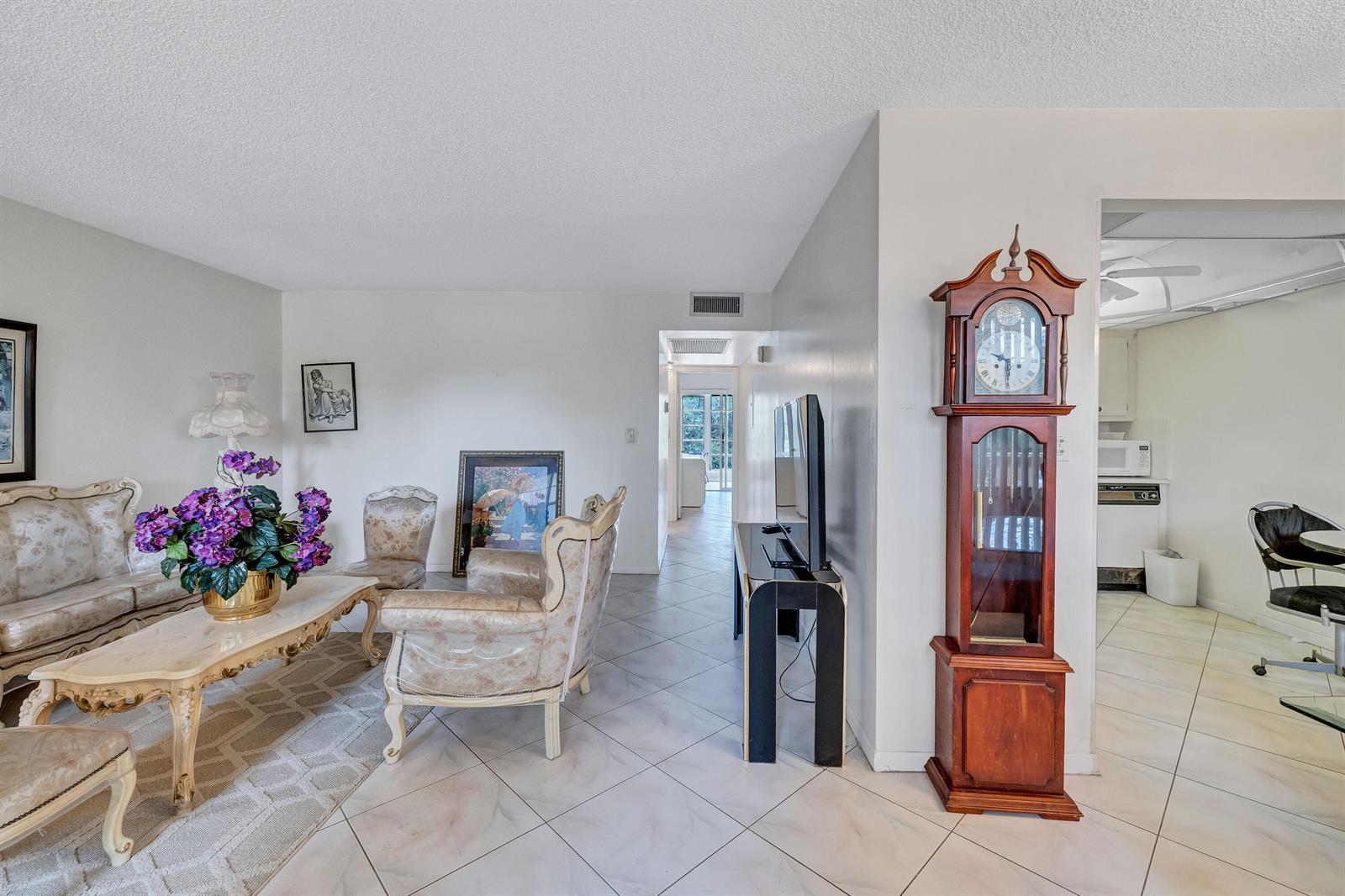 A living room features a grandfather clock, ornate furniture, a television console, and tile flooring — 1902 Bermuda Circle # L2, Coconut Creek FL 33066, COCONUT CREEK, FL