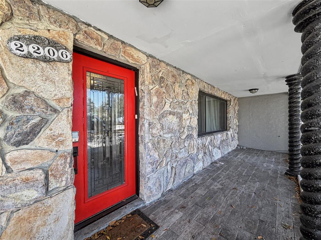 A red front door with a glass insert sits on a stone-faced porch — 2206 HOWARD LANE, TAMPA, FL