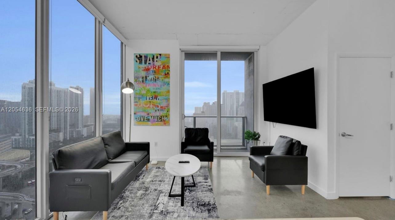 A modern living room features black leather furniture, a white coffee table, and floor-to-ceiling windows — 151 SE 1st St # 2411, Miami FL 33131, MIAMI, FL