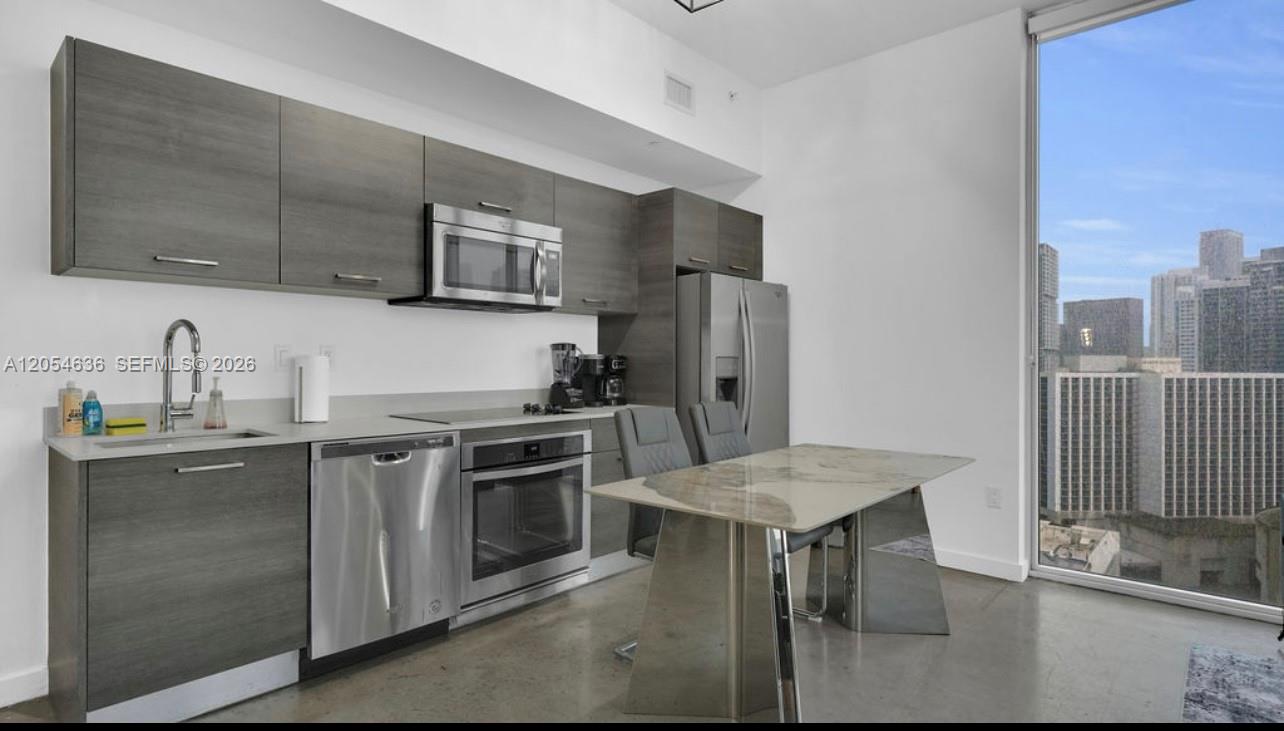 A modern kitchen features dark wood cabinetry, stainless steel appliances, and a dining table — 151 SE 1st St # 2411, Miami FL 33131, MIAMI, FL