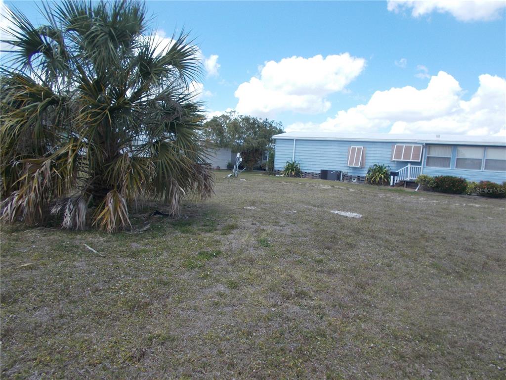 A light blue mobile home sits on a grassy lot with a large palm tree — 6517 KIPA COURT, NORTH PORT, FL