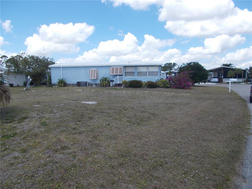 A light blue manufactured home sits on a grassy lot under a cloudy sky — 6517 KIPA COURT, NORTH PORT, FL