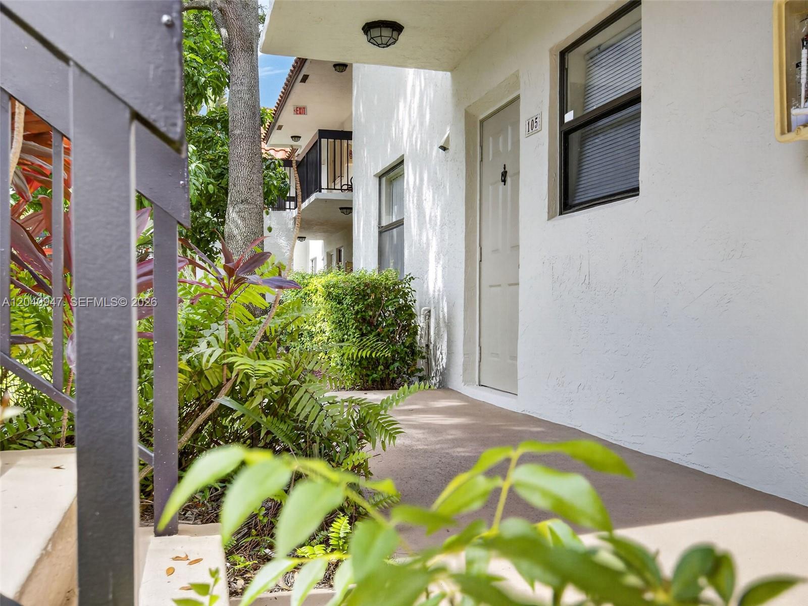 A ground-level apartment entrance features a white door numbered 105 and surrounding tropical landscaping — 15718 E Waterside Cir # 105, Sunrise FL 33326, SUNRISE, FL