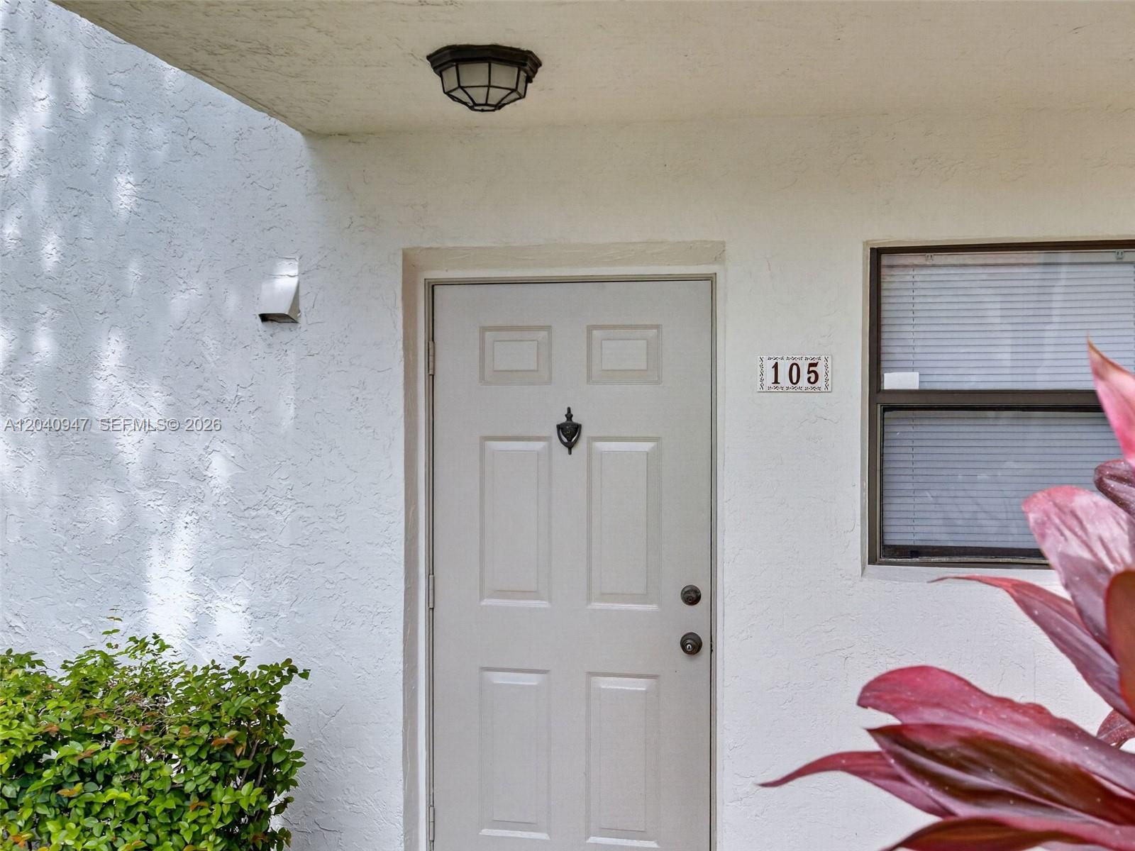 A white exterior door marked 105 is set in a textured wall with a window — 15718 E Waterside Cir # 105, Sunrise FL 33326, SUNRISE, FL