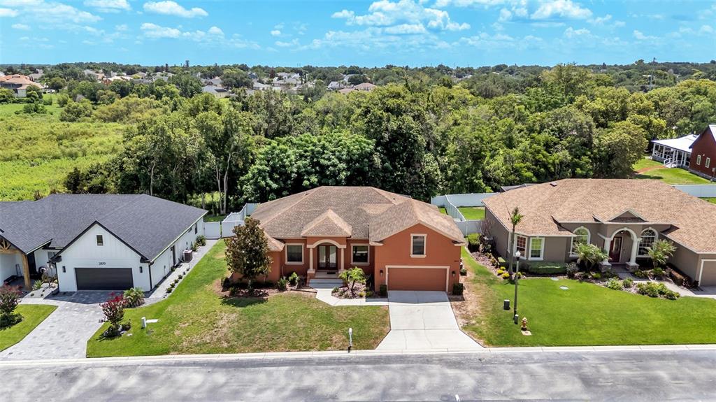 An aerial view shows three suburban houses with driveways and lawns against a wooded background — 2873 KINSLEY DRIVE, LAKELAND, FL