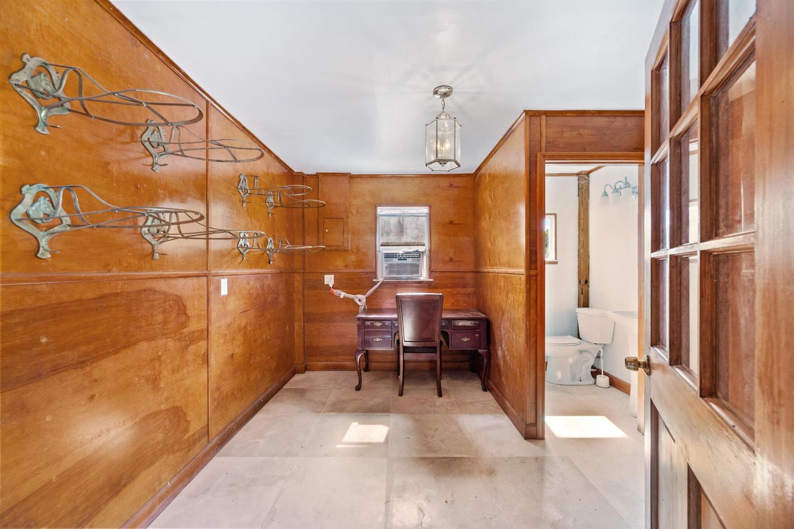 A wood-paneled room features a desk, wall-mounted racks, a window air conditioner, and an adjacent bathroom — 13717 E Citrus Drive, FL 33470, FL