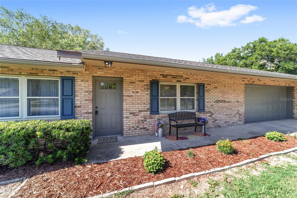 A brick house exterior features a gray front door, a garage, and a small bench — 4008 SE 61 PLACE, OCALA, FL