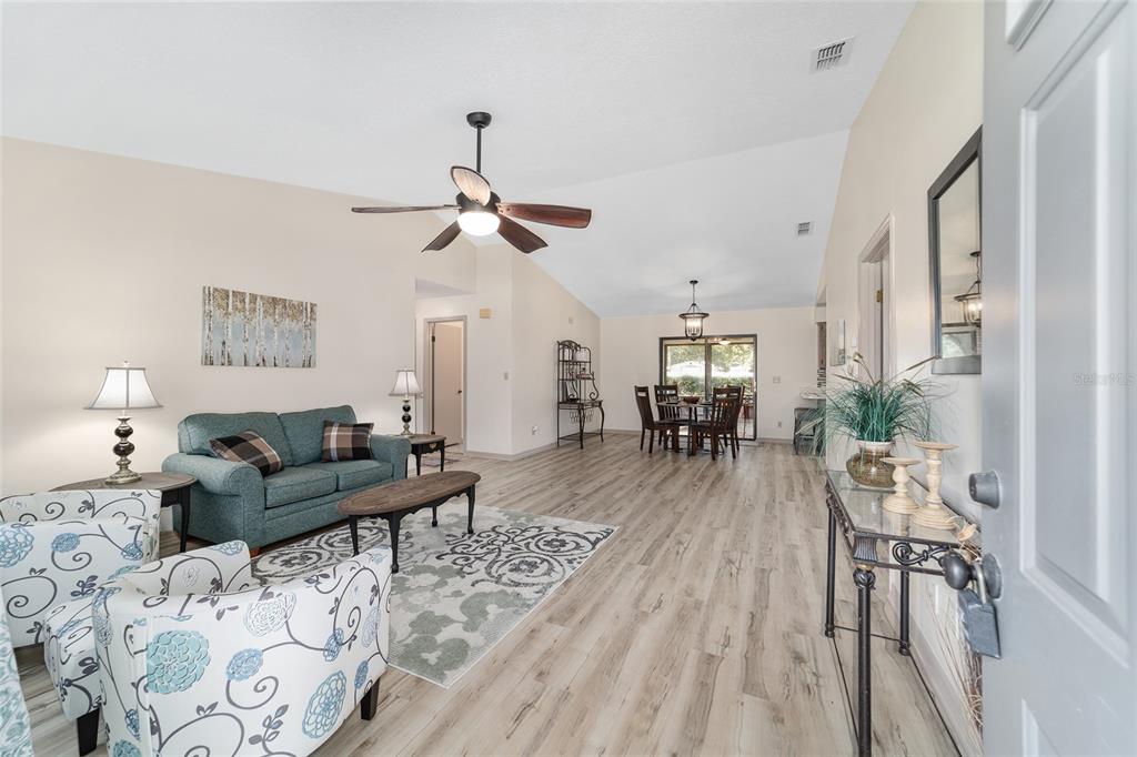 A bright open-concept living and dining area features wood-look flooring and a vaulted ceiling — 4008 SE 61 PLACE, OCALA, FL