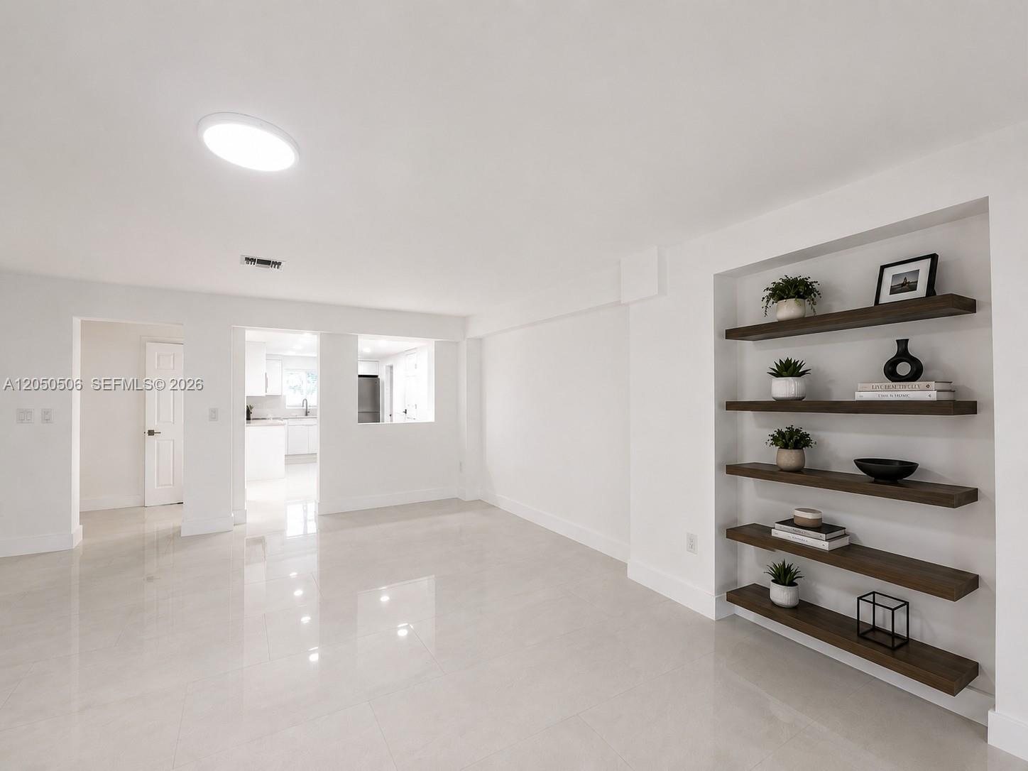 A bright, minimalist living area features white walls, glossy tile floors, and built-in wooden shelving — 5190 E 1st Ave # B, Hialeah FL 33013, HIALEAH, FL