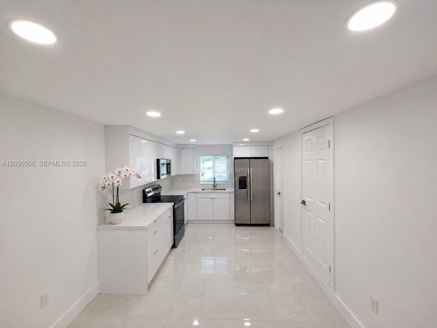 A modern, galley-style kitchen features white cabinetry, stainless steel appliances, and light-colored tile flooring — 5190 E 1st Ave # B, Hialeah FL 33013, HIALEAH, FL