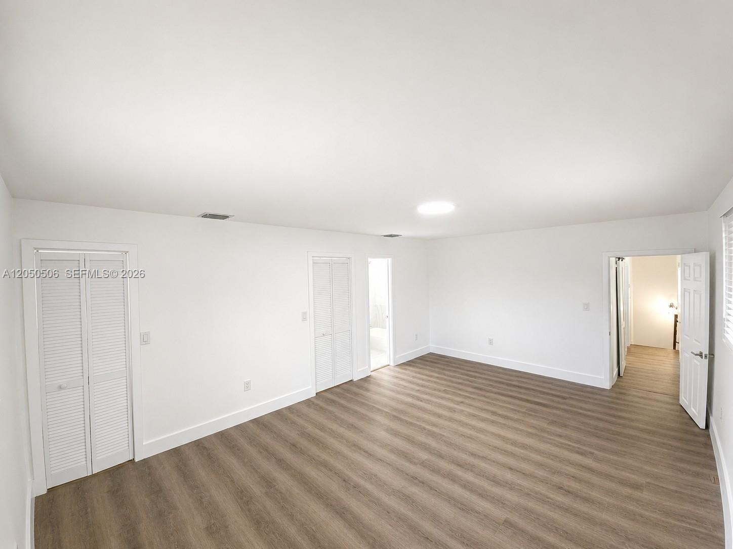 A bedroom with white walls, wood-look flooring, two sets of louvered closet doors, and doorways — 5190 E 1st Ave # B, Hialeah FL 33013, HIALEAH, FL
