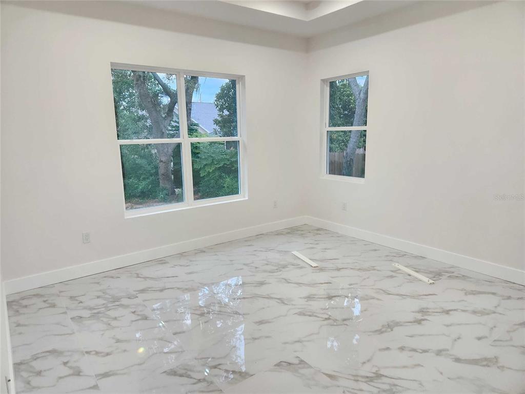 An empty room with white walls, a tray ceiling, and white marble-patterned tile flooring — 5413 DELTONA BOULEVARD, SPRING HILL, FL
