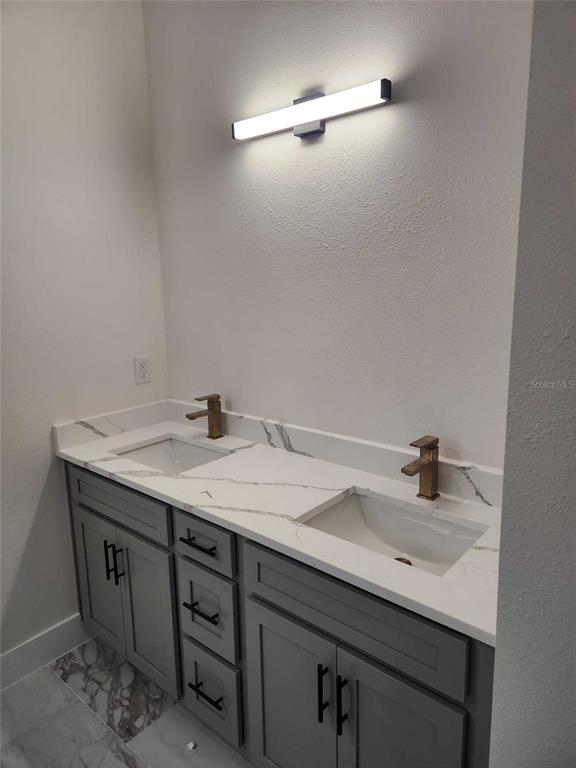 A bathroom vanity features a white marble countertop, dual sinks, bronze faucets, and gray cabinetry — 5413 DELTONA BOULEVARD, SPRING HILL, FL