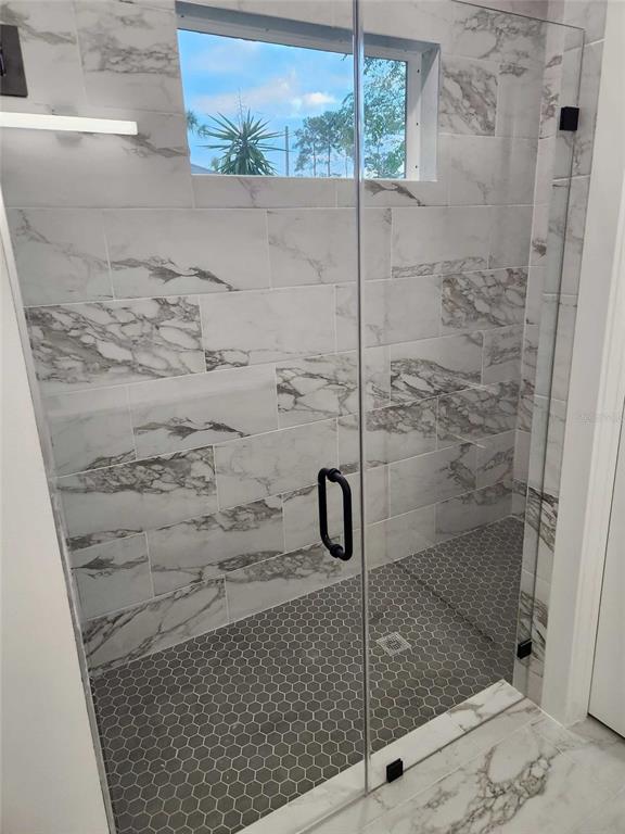 A walk-in shower features marble-look wall tiles, a gray hexagonal tile floor, and glass doors — 5413 DELTONA BOULEVARD, SPRING HILL, FL