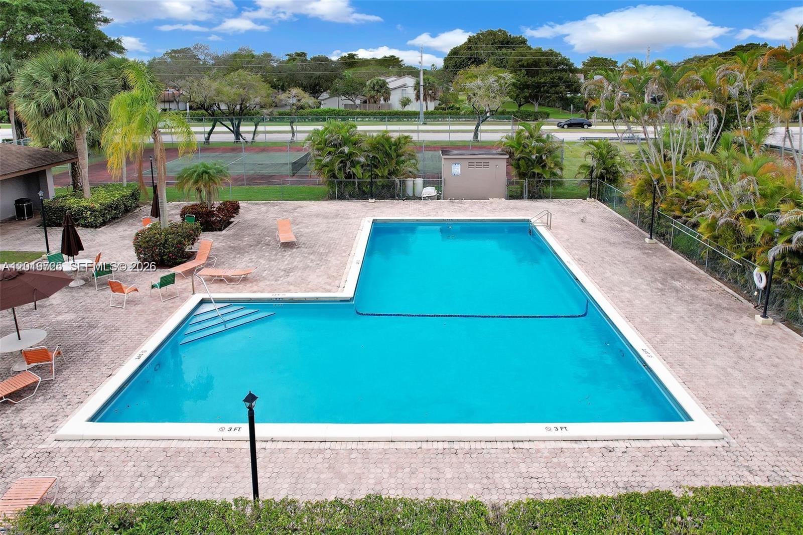 An aerial view of an L-shaped swimming pool surrounded by a paved deck and landscaping — 10825 SW 112 AV # 215, Miami FL 33176, MIAMI, FL
