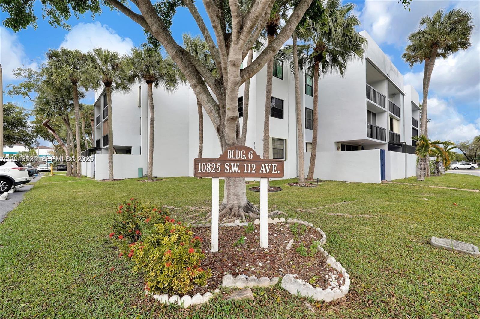 A white multi-story apartment building stands behind a wooden sign in a grassy yard — 10825 SW 112 AV # 215, Miami FL 33176, MIAMI, FL