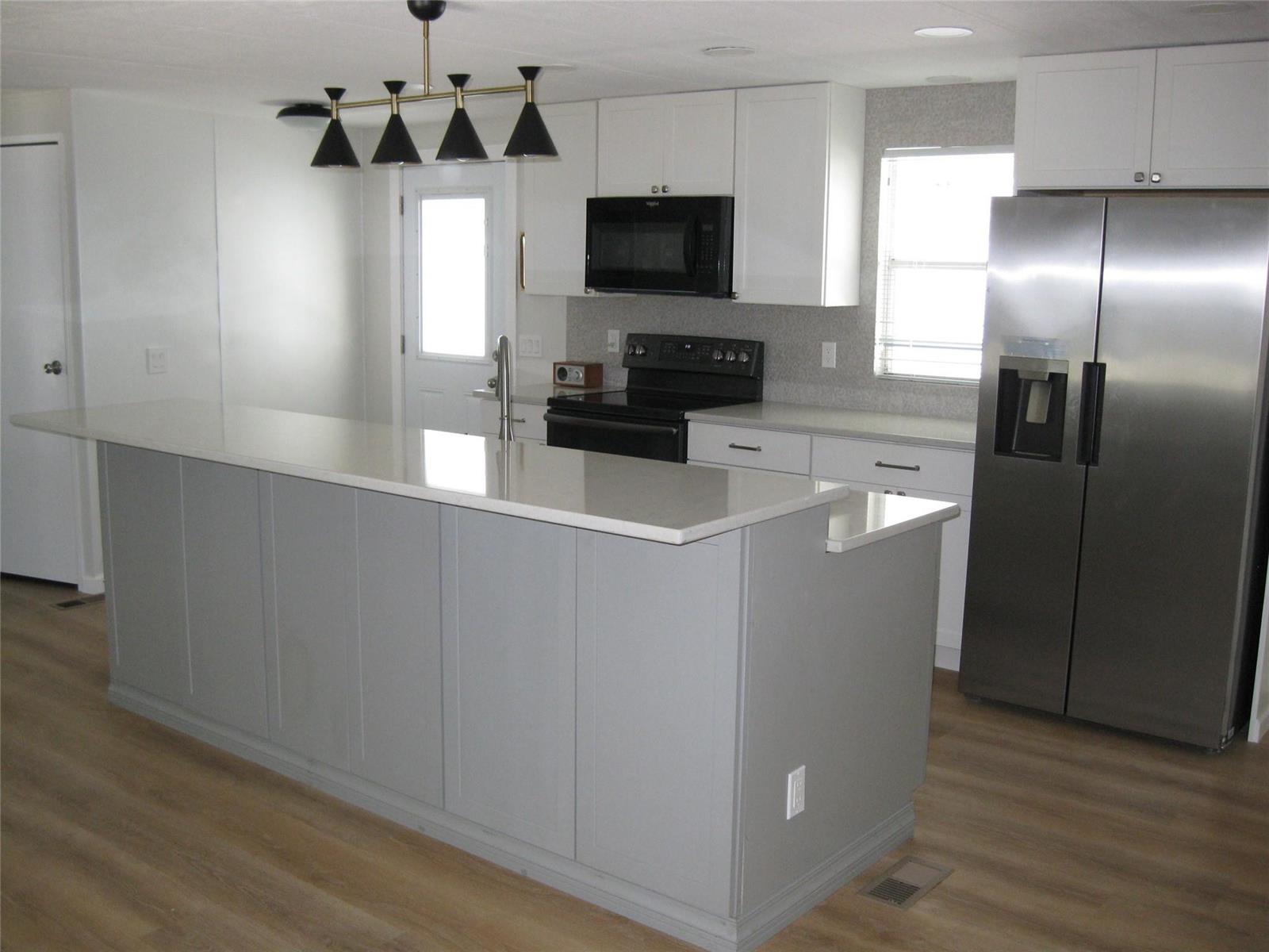 A kitchen features a gray island, white cabinets, stainless steel appliances, and light wood flooring — 4800 SE Federal Highway, Stuart FL 34997, STUART, FL