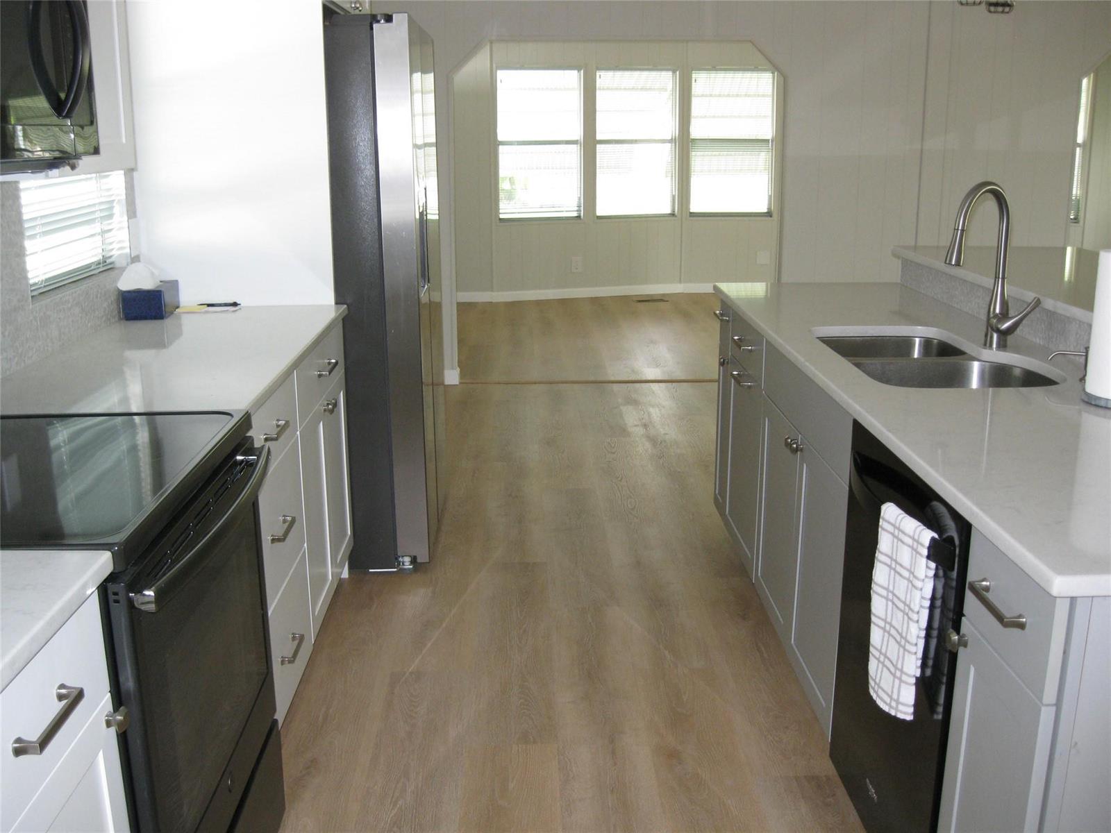 A kitchen with gray cabinets, stainless steel appliances, and light wood flooring leads to a room — 4800 SE Federal Highway, Stuart FL 34997, STUART, FL