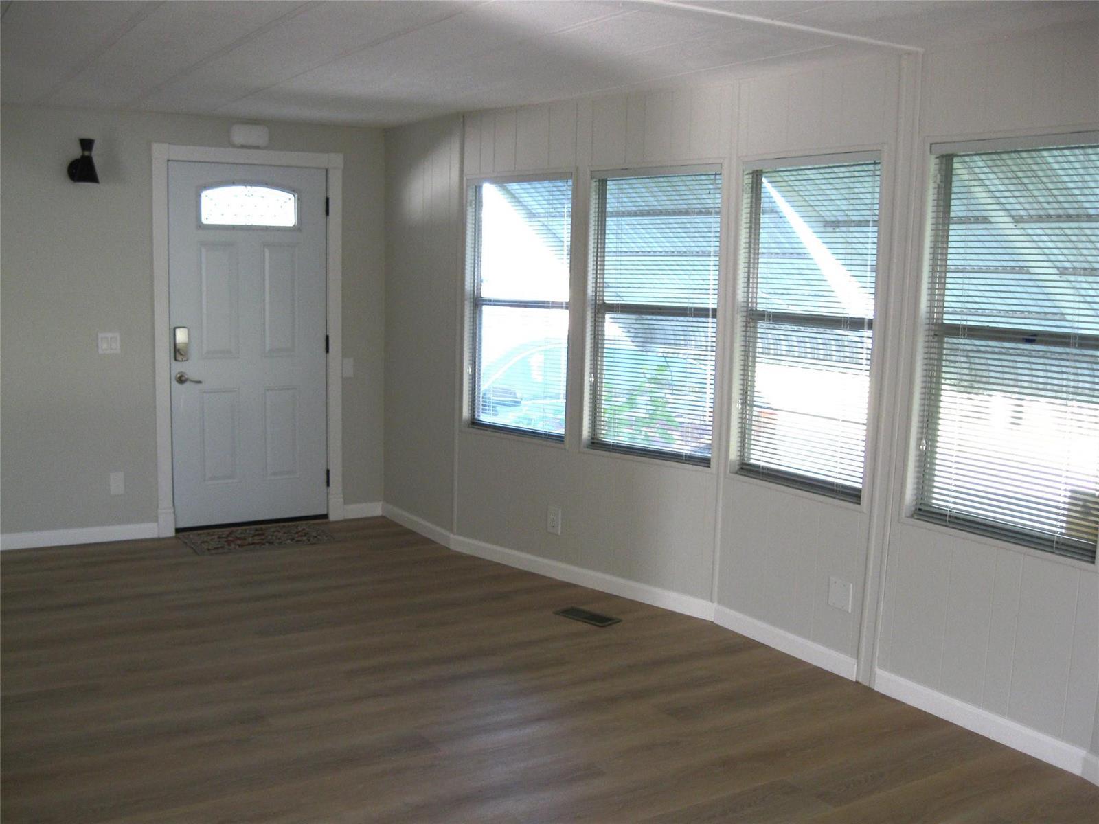 An empty room features light-colored wood-look flooring, white walls, a front door, and several windows — 4800 SE Federal Highway, Stuart FL 34997, STUART, FL
