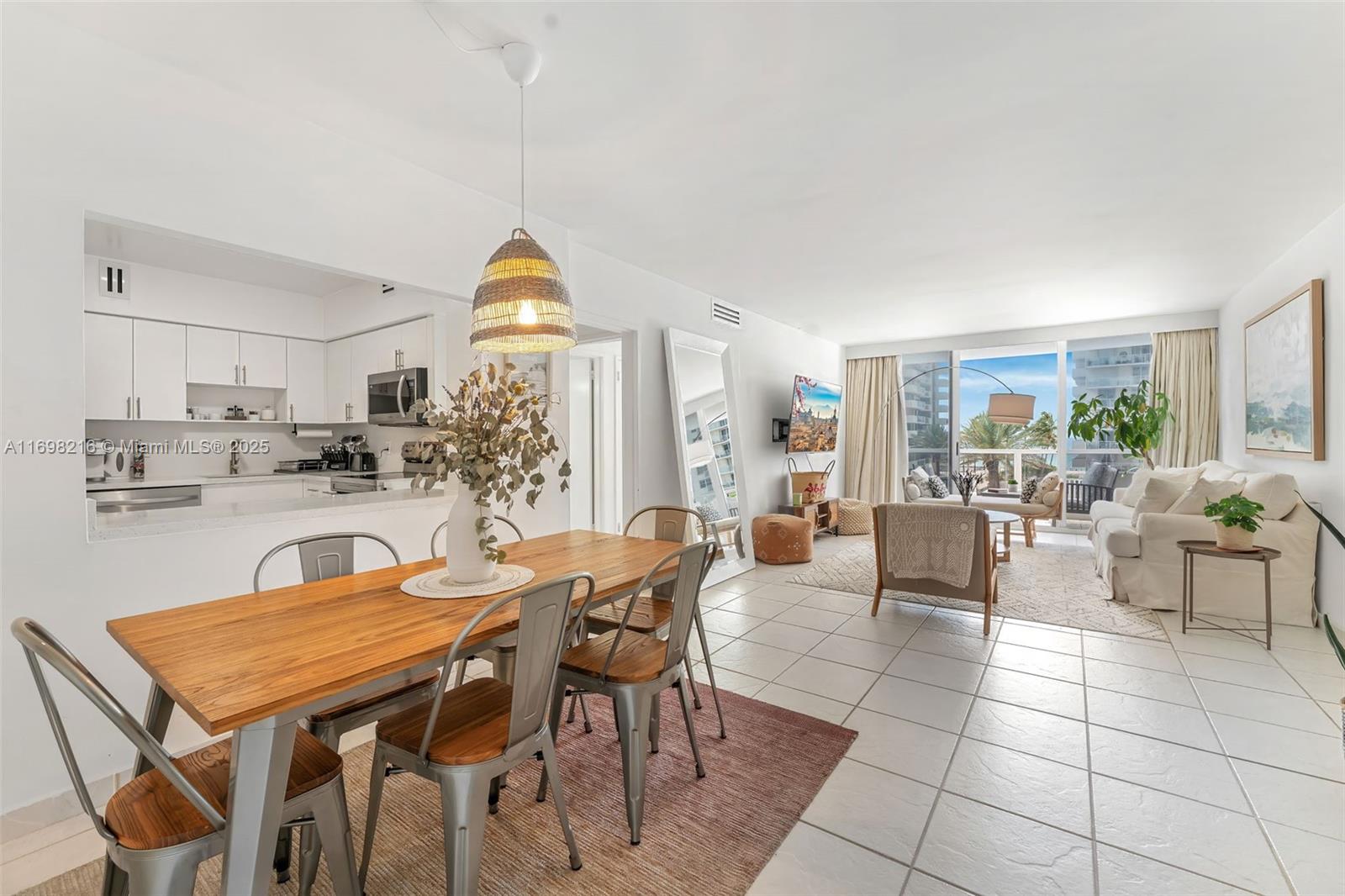 An open-concept living and dining area features a wooden table, white kitchen, and balcony view — 5700 Collins Ave # 5B, Miami Beach FL 33140, MIAMI BEACH, FL