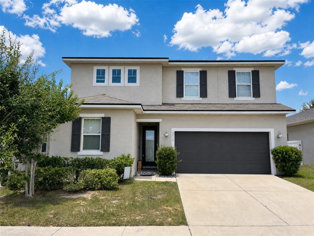 A two-story suburban house with a beige stucco exterior, dark shutters, and a two-car garage — 324 BUCHANNAN DRIVE, DAVENPORT, FL