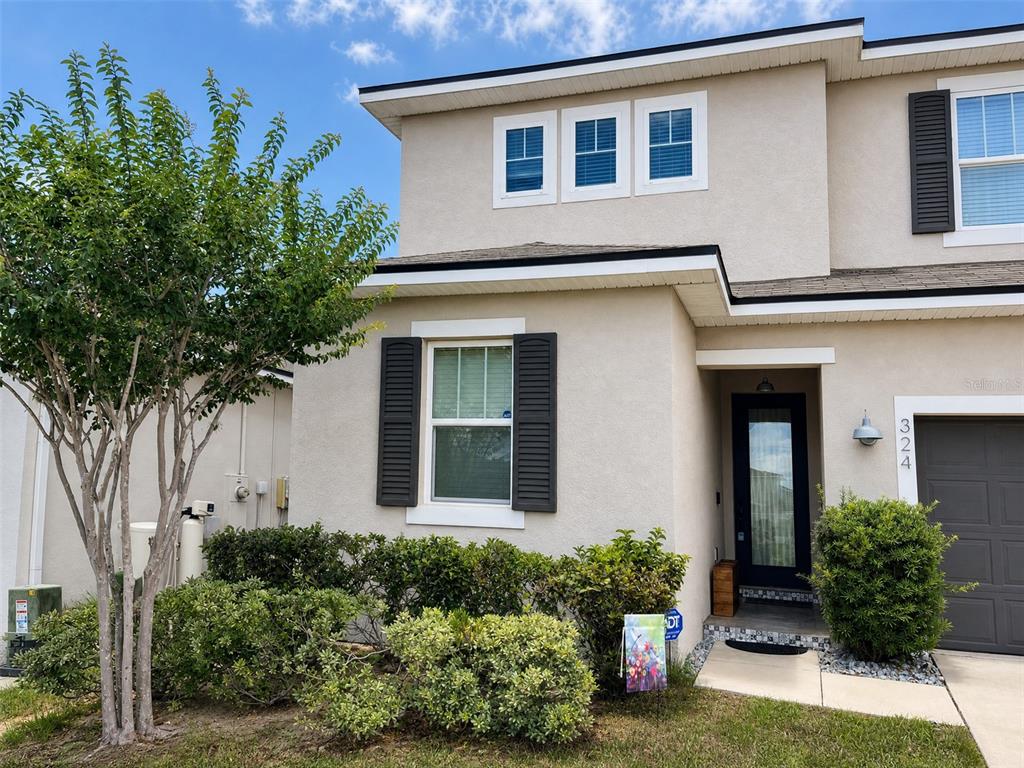 A two-story house exterior features beige stucco, dark shutters, a front door, and landscaping — 324 BUCHANNAN DRIVE, DAVENPORT, FL
