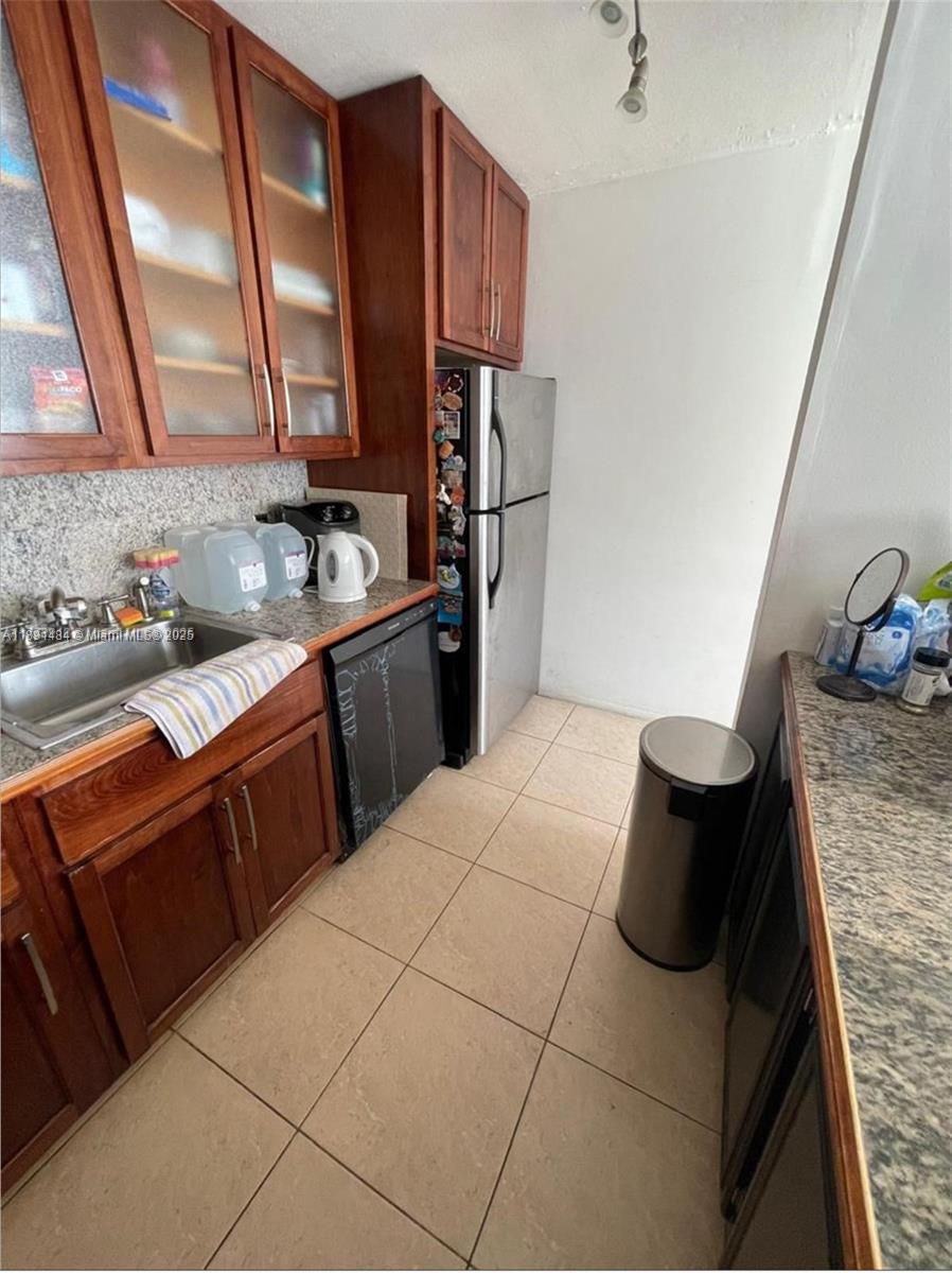 A kitchen features wood cabinets, granite countertops, a stainless steel refrigerator, and tiled flooring — 9460 Live Oak Pl # 309, Davie FL 33324, DAVIE, FL