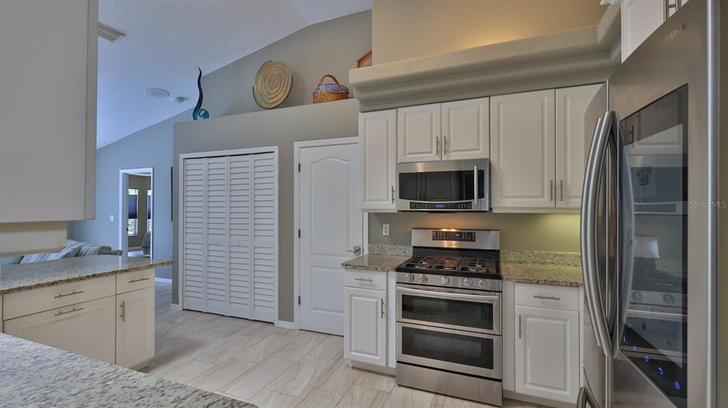 A kitchen features white cabinets, stainless steel appliances, granite countertops, and light-colored tile flooring — 29 ACCLAIM AT LIONSPAW, DAYTONA BEACH, FL