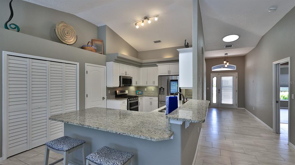 A kitchen with white cabinets, granite countertops, and a breakfast bar overlooks a tiled hallway — 29 ACCLAIM AT LIONSPAW, DAYTONA BEACH, FL