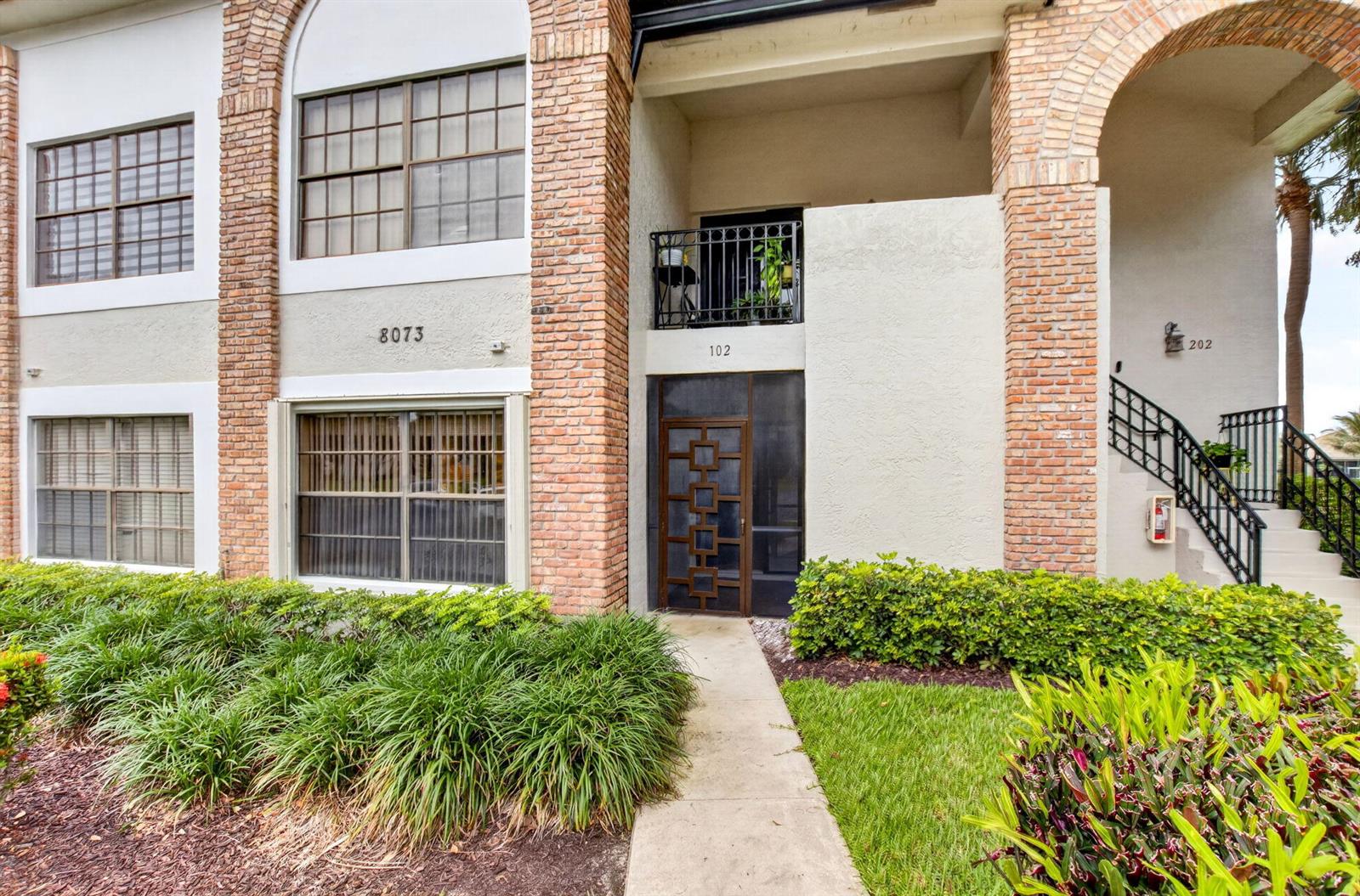 The exterior of a multi-story building features brick accents, a ground-floor entrance, and a balcony — 8073 Aberdeen Drive # 102, Boynton Beach FL 33472, BOYNTON BEACH, FL