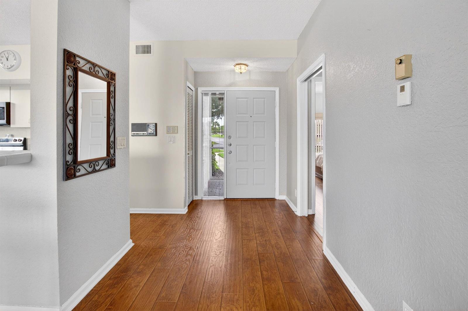 A bright entryway features wood-look flooring, a white front door, and a decorative wall mirror — 8073 Aberdeen Drive # 102, Boynton Beach FL 33472, BOYNTON BEACH, FL