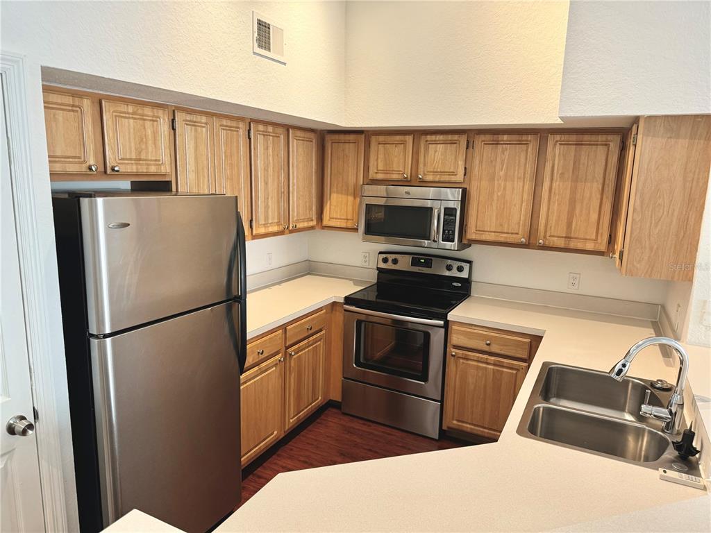 A kitchen features light wood cabinets, stainless steel appliances, and white countertops — 13028 PLANTATION PARK CIRCLE UNIT 1226, ORLANDO, FL