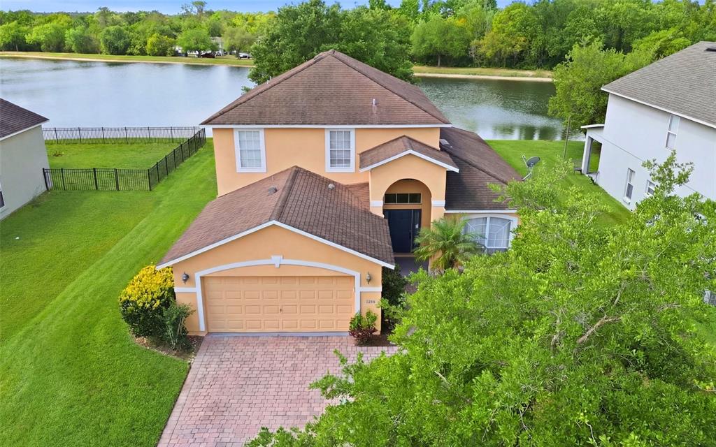 An aerial view of a two-story peach-colored house with a brick driveway and lakefront backyard — 2838 SWEETSPIRE CIRCLE, KISSIMMEE, FL