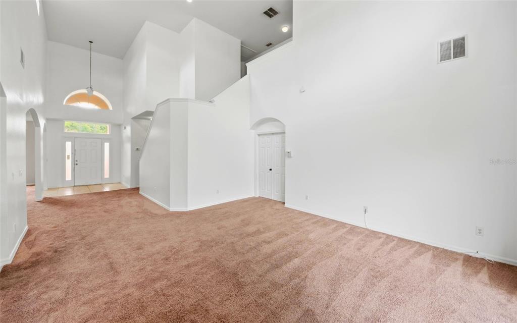 A spacious, high-ceilinged living room features brown carpeting, white walls, and a front entryway — 2838 SWEETSPIRE CIRCLE, KISSIMMEE, FL